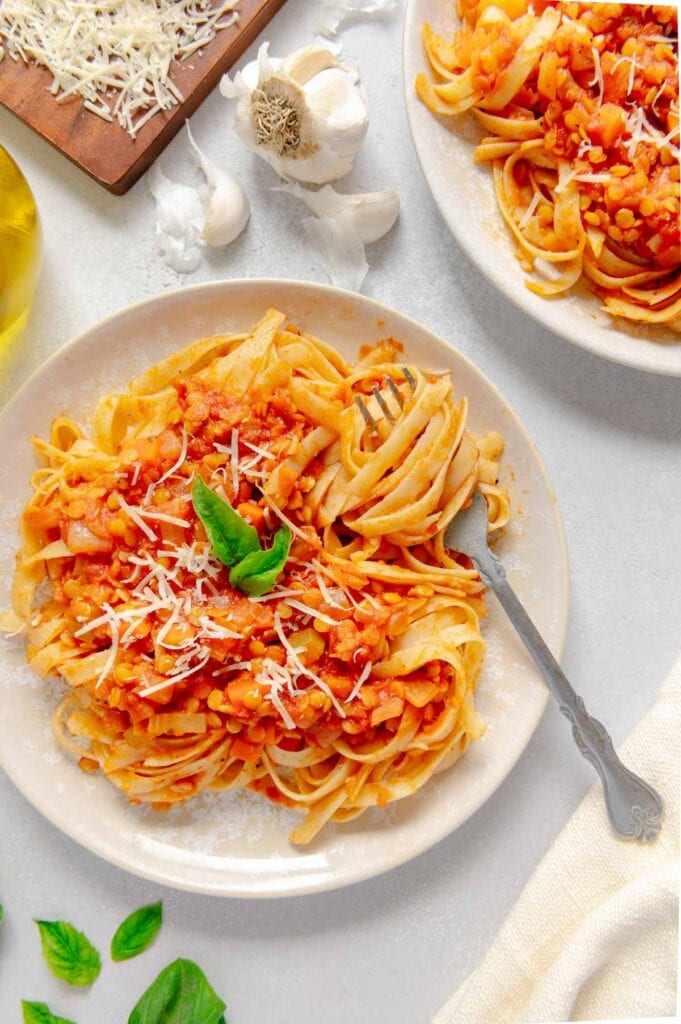 A fork swirling a forkful of red lentil bolognese sauce.