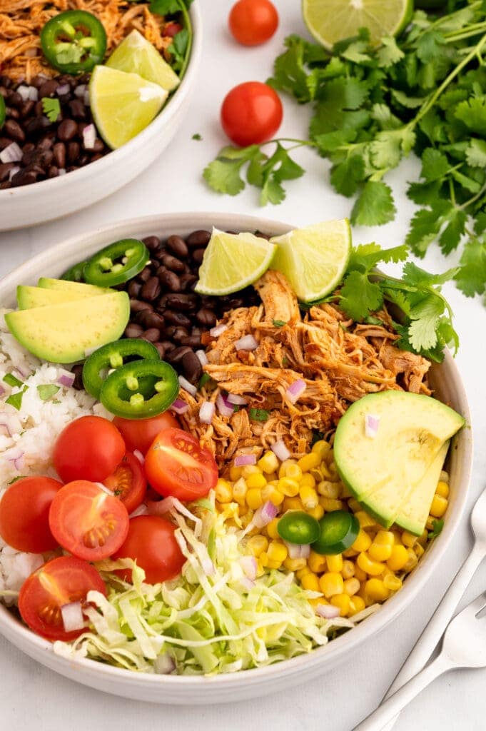 crockpot salsa chicken in a large white bowl with other veggies next to a bundle of cilantro