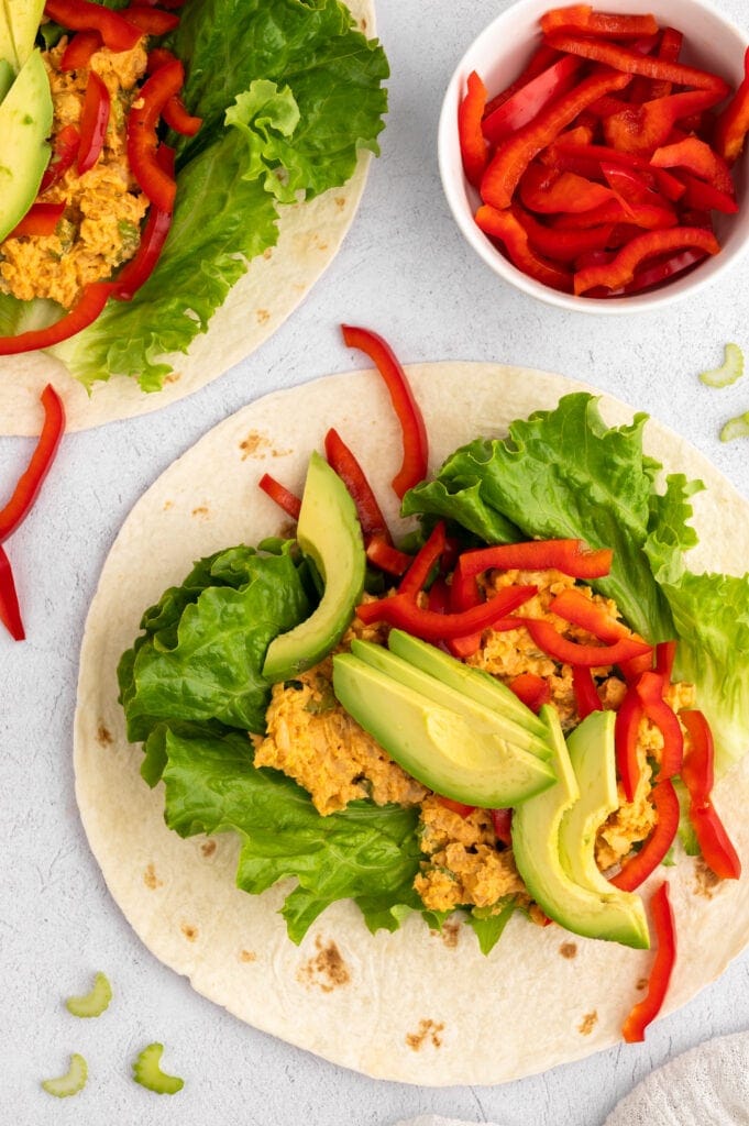 Overhead view of a Buffalo Chickpea Wrap before being wrapped next to a bowl of sliced red peppers.