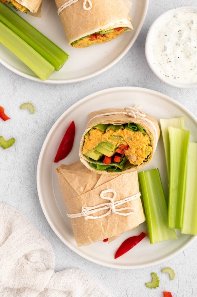 Overhead view of two plates with Buffalo Chickpea Wraps on them next to celery and a small dish of dipping sauce.