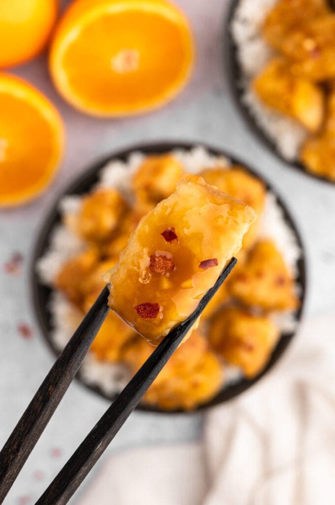 holding a piece of orange chicken with chopsticks
