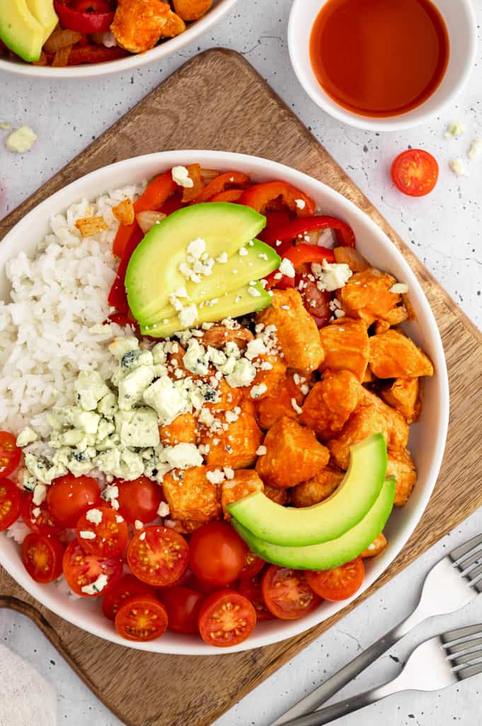 a large buffalo chicken rice bowl next to two forks on a cutting board.