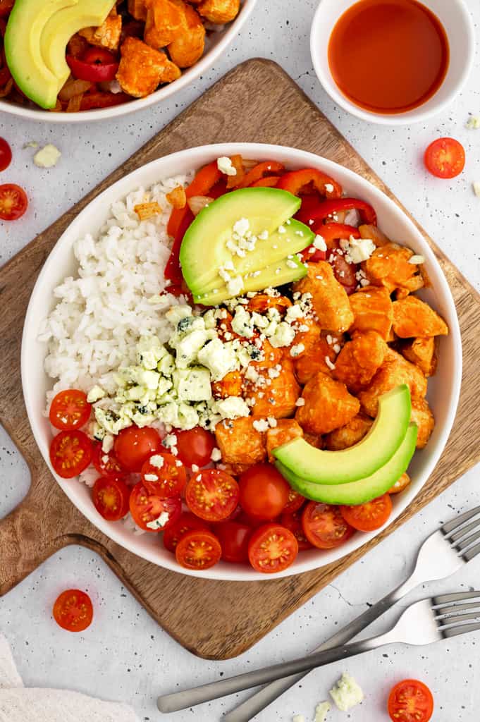 a large buffalo chicken rice bowl on a cutting board next to forks and sauce.