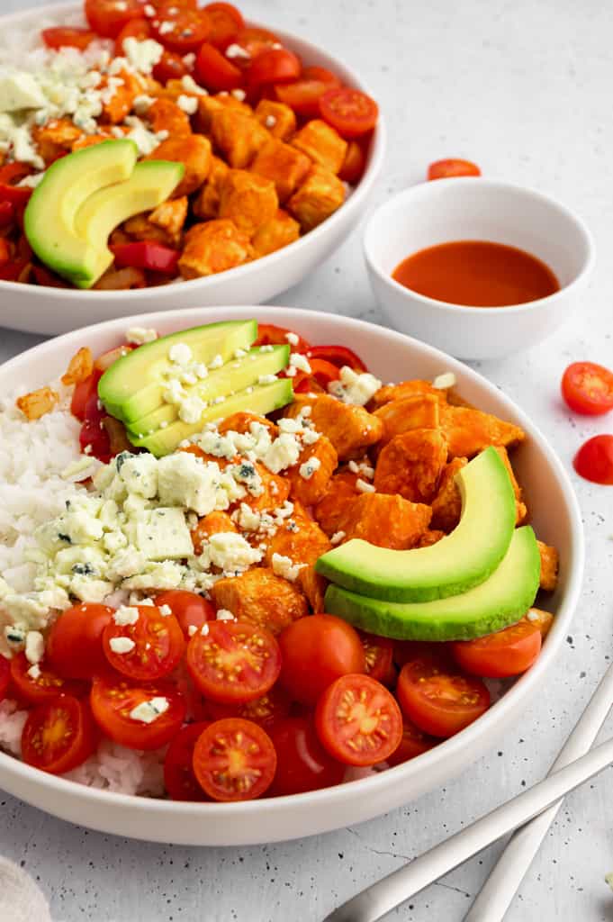 two buffalo chicken rice bowls next to a ramekin of buffalo sauce.
