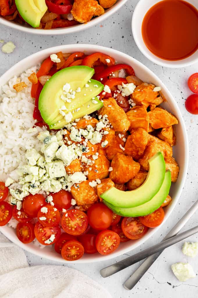 Buffalo chicken bowl with avocado, rice, tomatoes, and cheese.