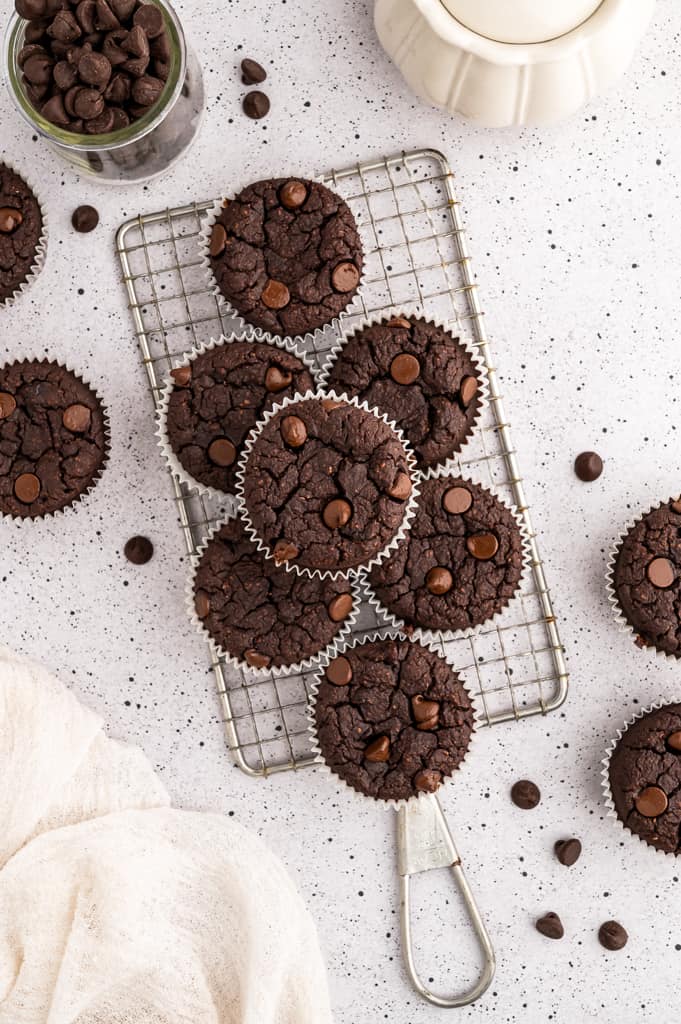 Stack of chocolate protein muffins on a wire cooling rack next to chocolate chips in a jar.