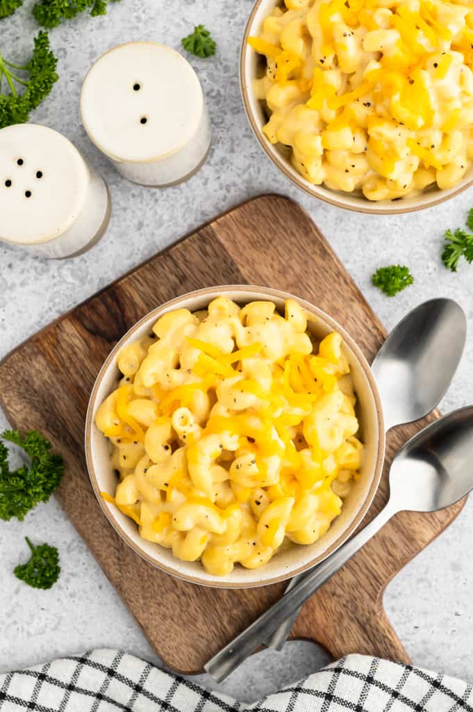 Top view of high protein mac and cheese in a white bowl sitting on a cutting board next to spoons.