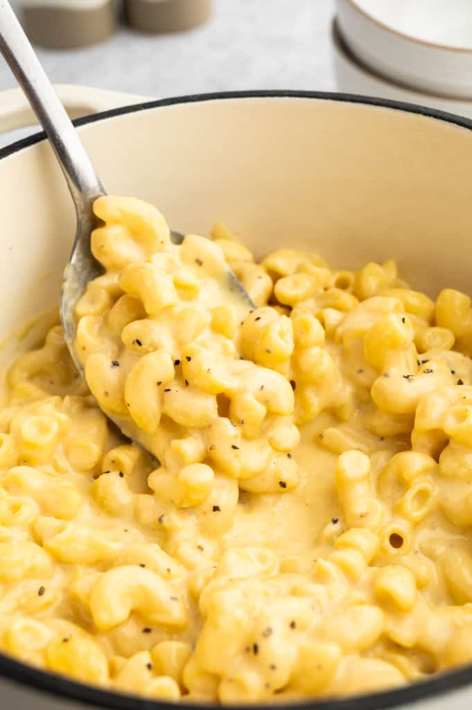 Using a big spoon to scoop out the mac and cheese from the pot.