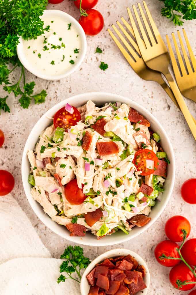 A bowl of BLT chicken salad next to forks and dressing.