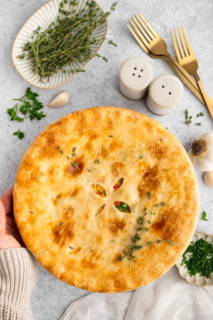 Freshly baked chicken pot pie next to fresh herbs.