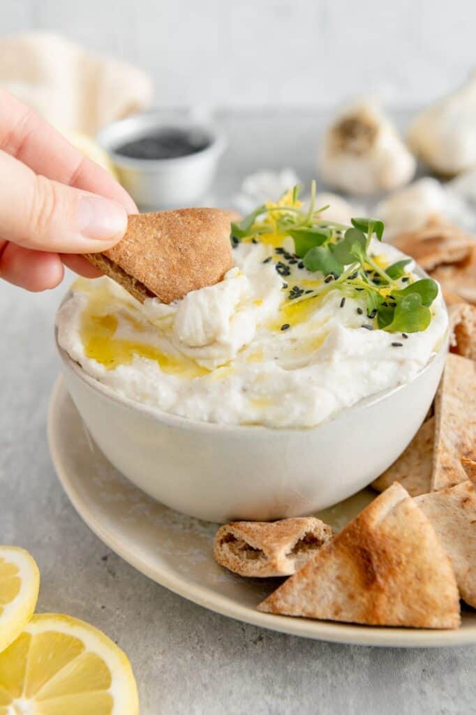 Toasted pita bread being dipped in a feta dip.