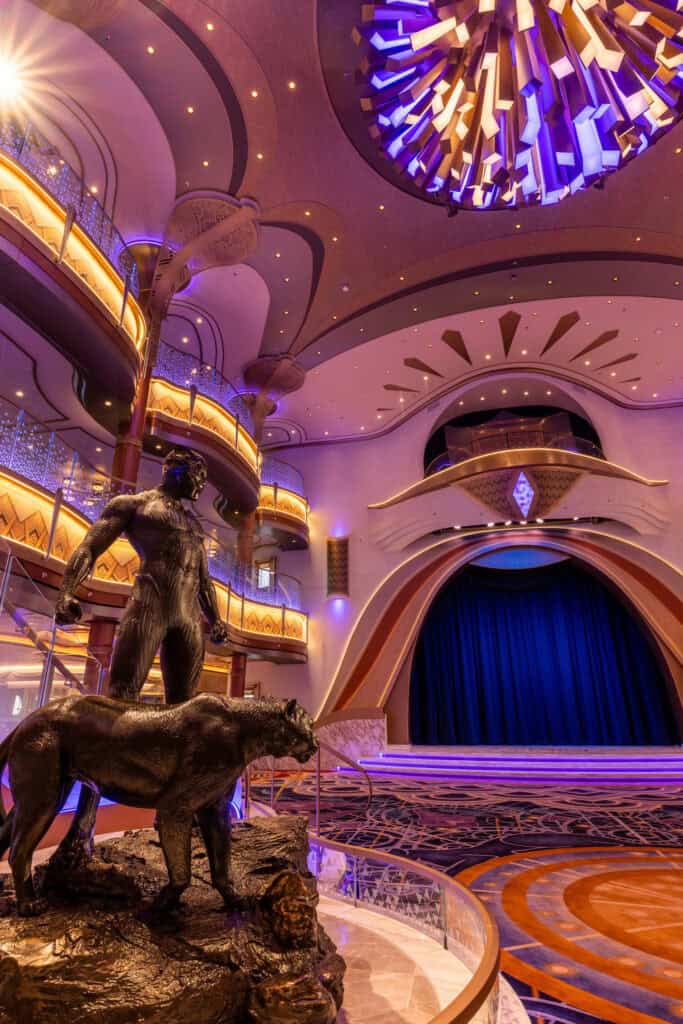 Elegant cruise ship theater with vibrant lighting and ornate decor.