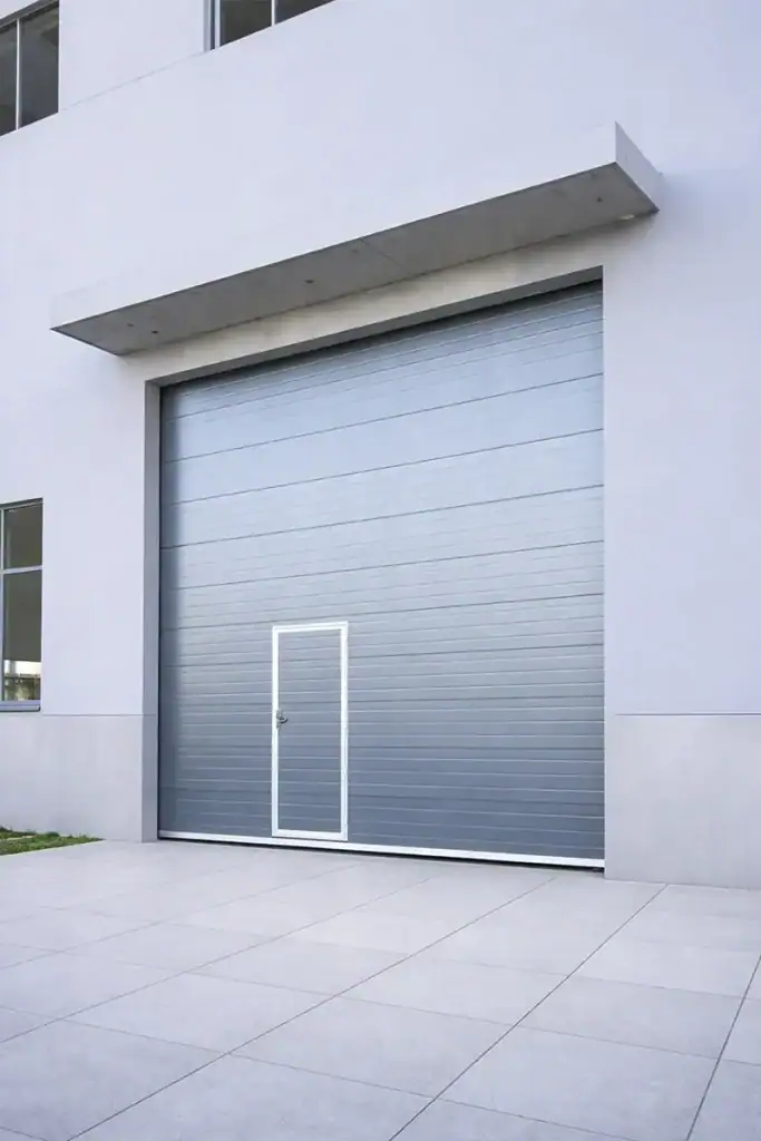Modern commercial sectional door with a seamlessly integrated wicket door, enhancing the exterior facade of a contemporary industrial building.