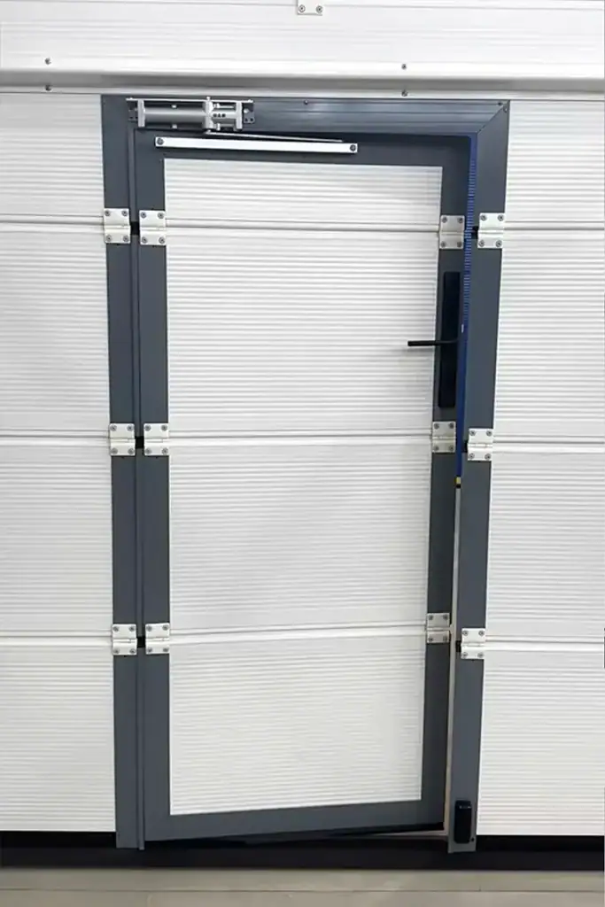 Close-up of a built-in wicket door on modern sectional doors, featuring heavy-duty hinges and a door closer for secure pedestrian access