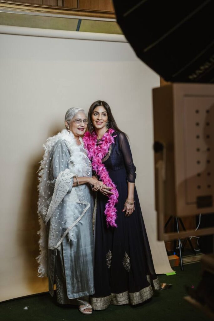 Two women in Indian outfits with feather boas posing at the white studio booth backdrop