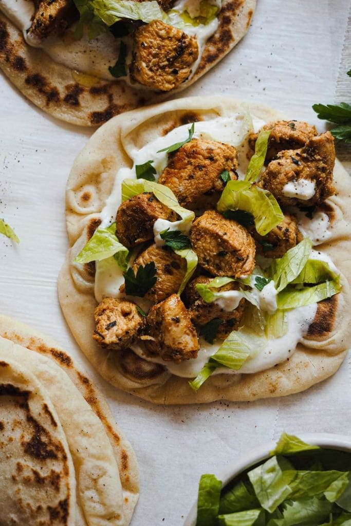 Paula's Apron Wrap de Pollo con Salsa de Queso Crema Este Wrap de Pollo con Salsa de Queso Crema os dejará alucinados! Pechugas de pollo deliciosamente marinadas con hierbas mediterráneas y un toque picante y ahumado... Buenísimo a más no poder! Y la salsa de queso crema es simplemente increíble! Combina muy bien con el pan y el pollo, y es un dip excelente e incluso un aliño genial para ensaladas! En esta foto cenital se ven dos panes planos con las capas del relleno del wrap: salsa de queso crema, pollo, lechuga y perejil. Abajo a la izquierda hay otro pan doblado por la mitad y arriba a la izquierda se ve un trozo de otro pan plano con todos los ingredientes. Abajo en la esquina izquierda se aprecia un trocito de un bol con lechuga.