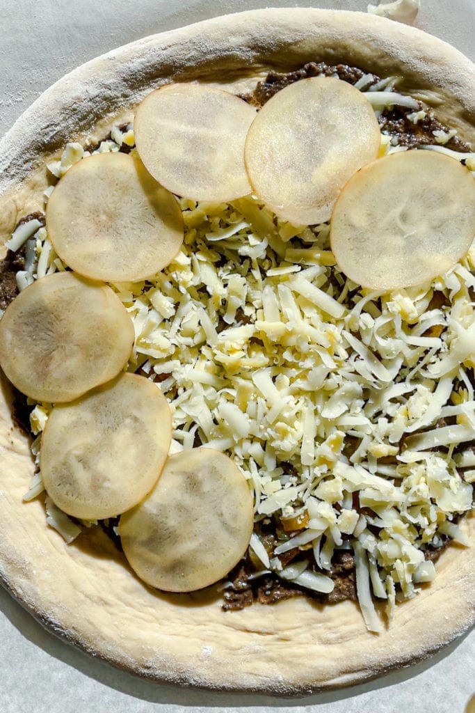Paula's Apron Pizza de Patata y Burrata con Trufa Pizza de Patata y Burrata con Trufa antes de hornearla, con la capa de patata a medio poner para que se vea la capa de cheddar y cebolla caramelizada. ¡Para morirse de buena! | Receta de Paula's Apron