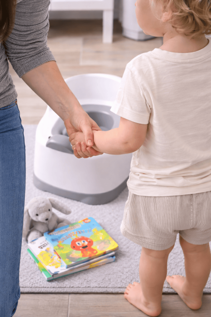 Close-up of mom holding toddler’s hand near potty chair