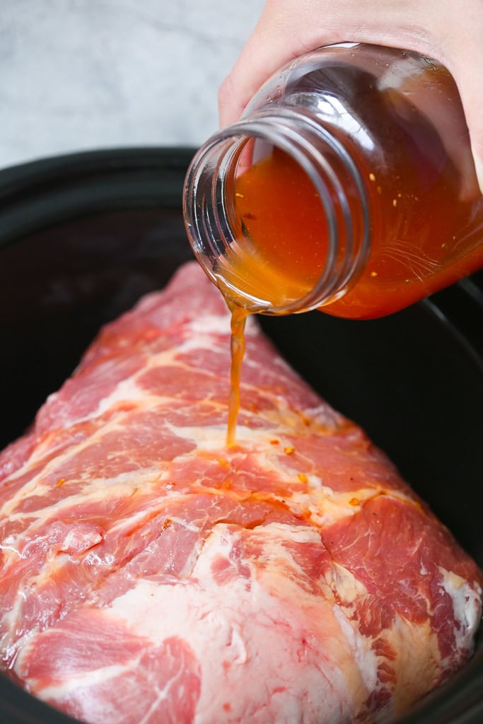 Carolina style vinegar based barbecue sauce pouring over boston butt in slow cooker