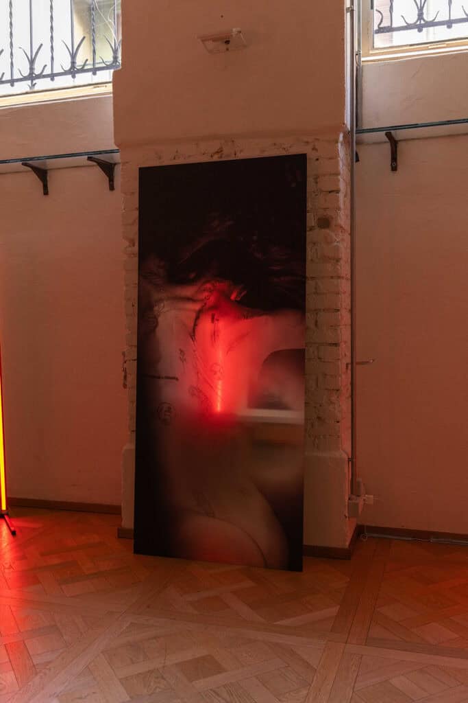 Large-scale photograph with red-tinted lighting displayed in a dim gallery space as part of Cate Colapietro’s “Breath Not Found” exhibition.