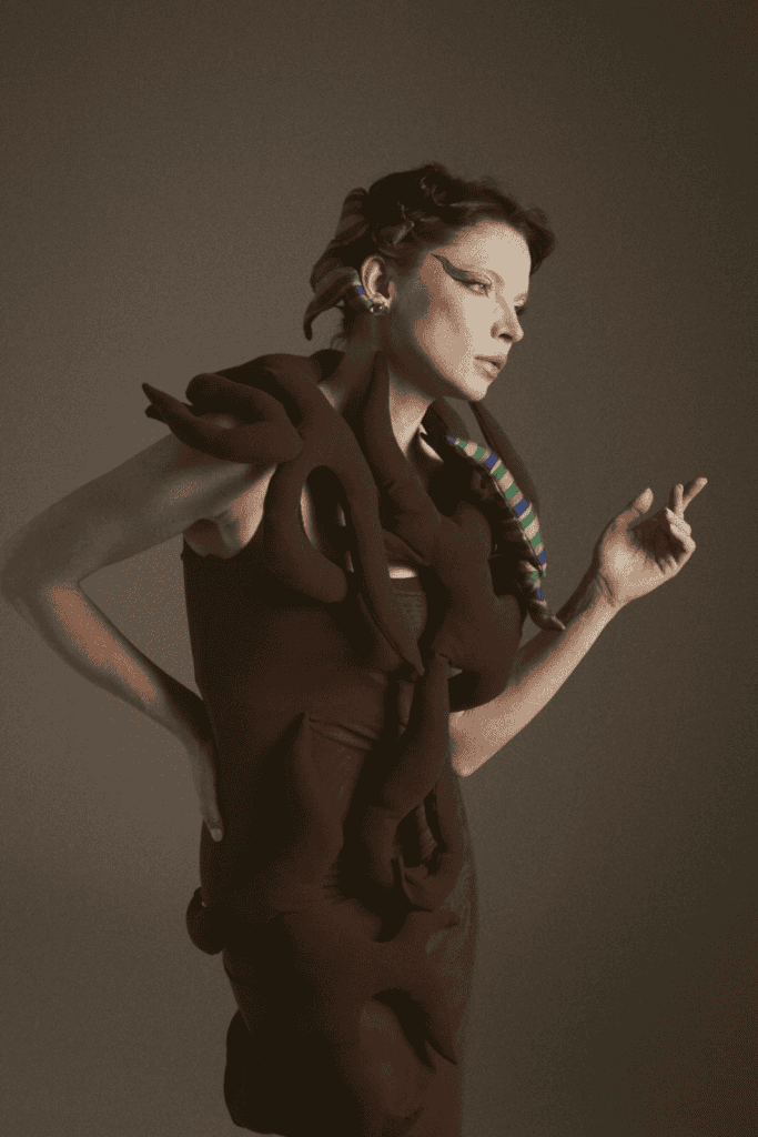 An editorial profile shot of a model wearing a dark No.sugar garment adorned with intertwined fabric "roots," highlighting the brand's focus on organic shapes and Uzbek heritage.