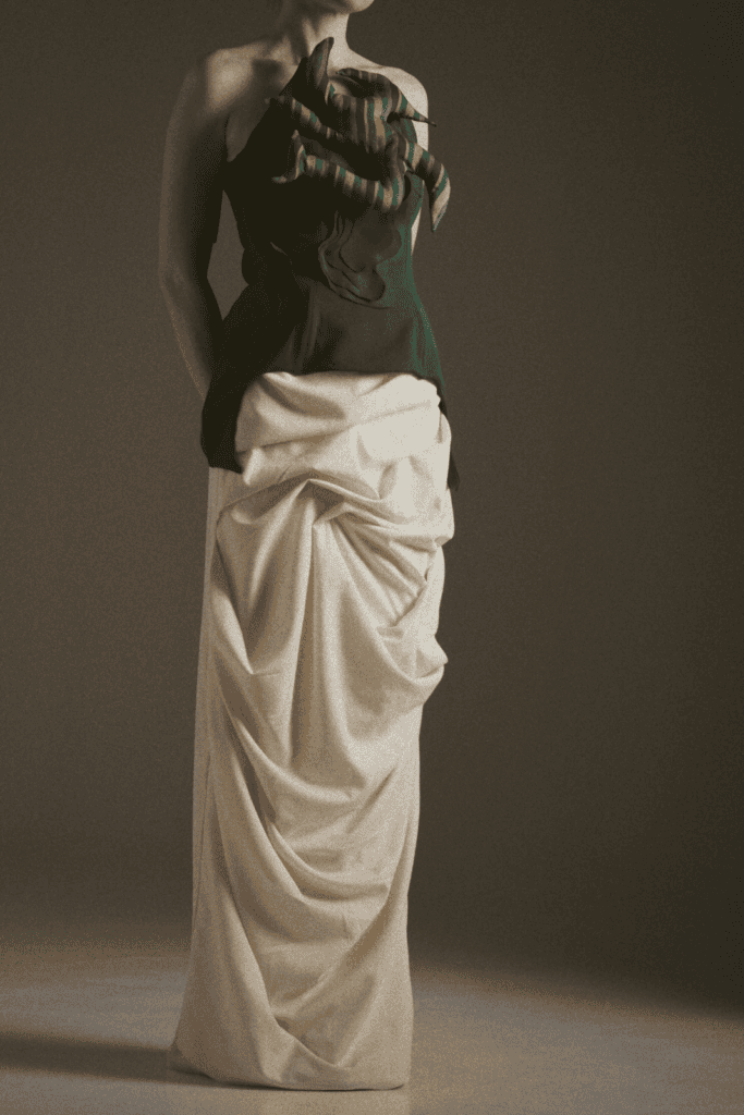 A studio shot of a No.sugar design featuring a dark strapless bodice with striped root accents paired with a voluminous, draped cream-colored floor-length skirt.