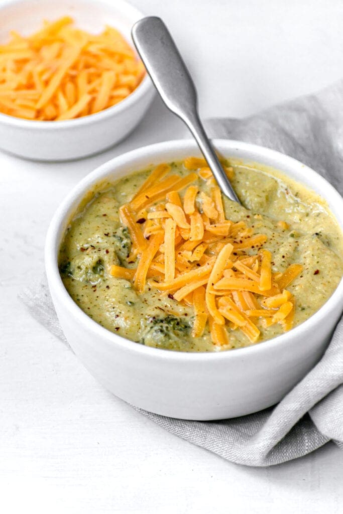side view of a bowl of instant pot broccoli cheddar soup topped with cheddar cheese