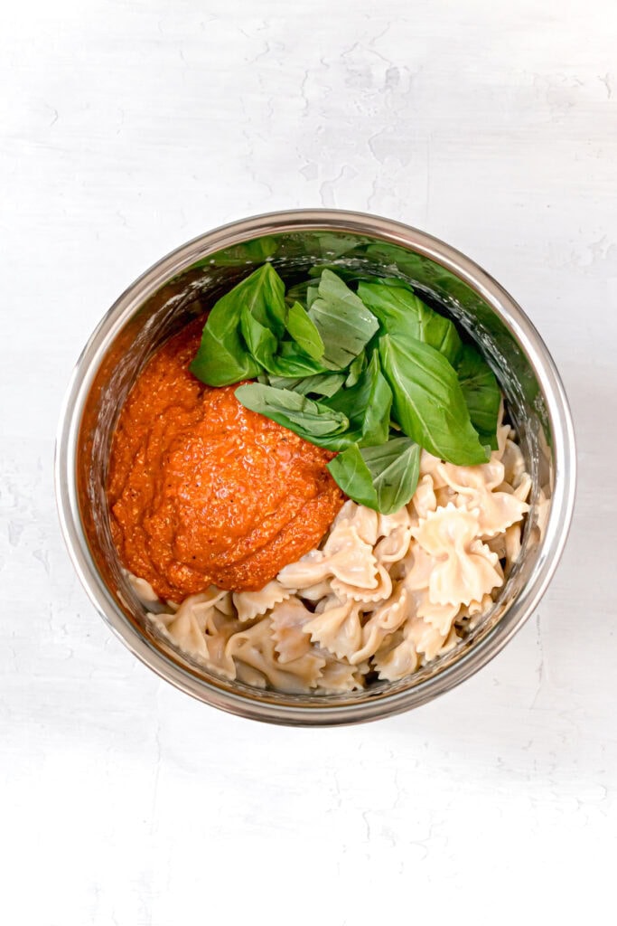 red pepper sauce with basil and pasta noodles in a mixing bowl