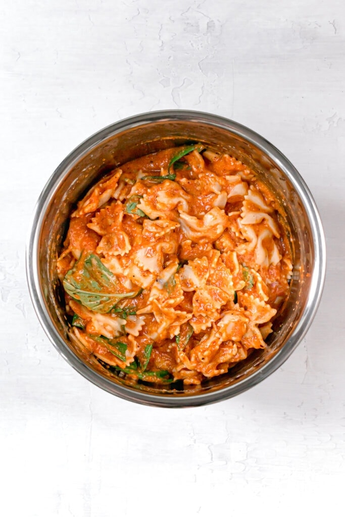 cooked pasta tossed in red pepper sauce in mixing bowl