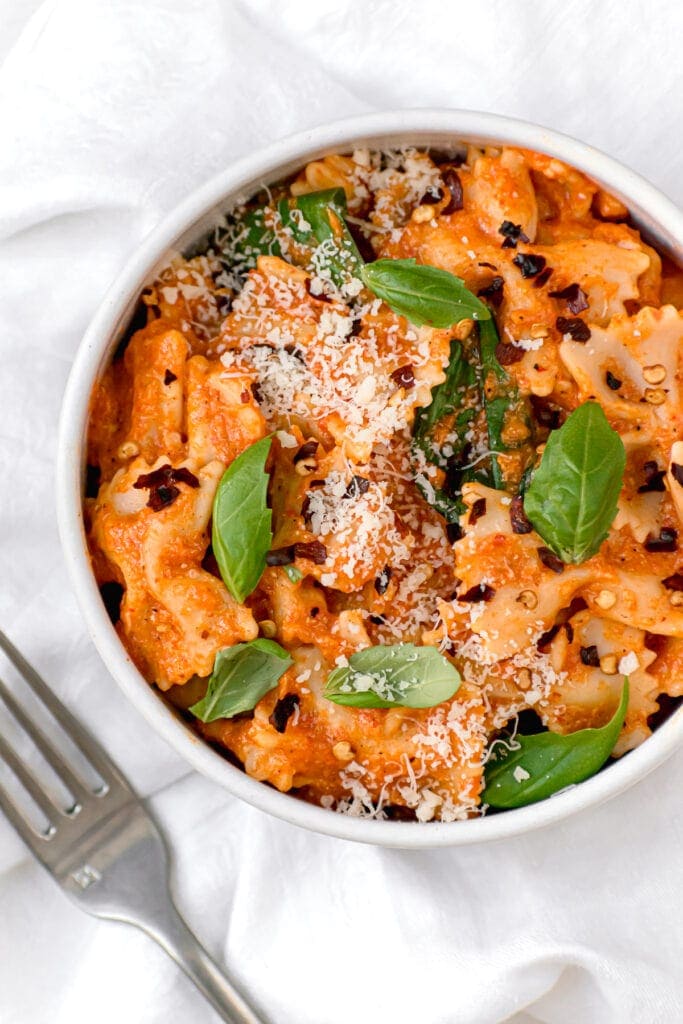 close up of red pepper pasta in a white bowl next to fork