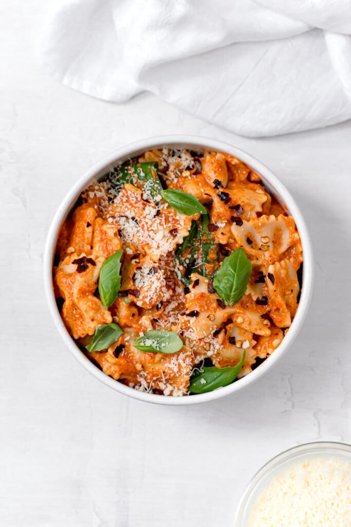 bowl of pasta tossed in red pepper sauce with cheese and garnish
