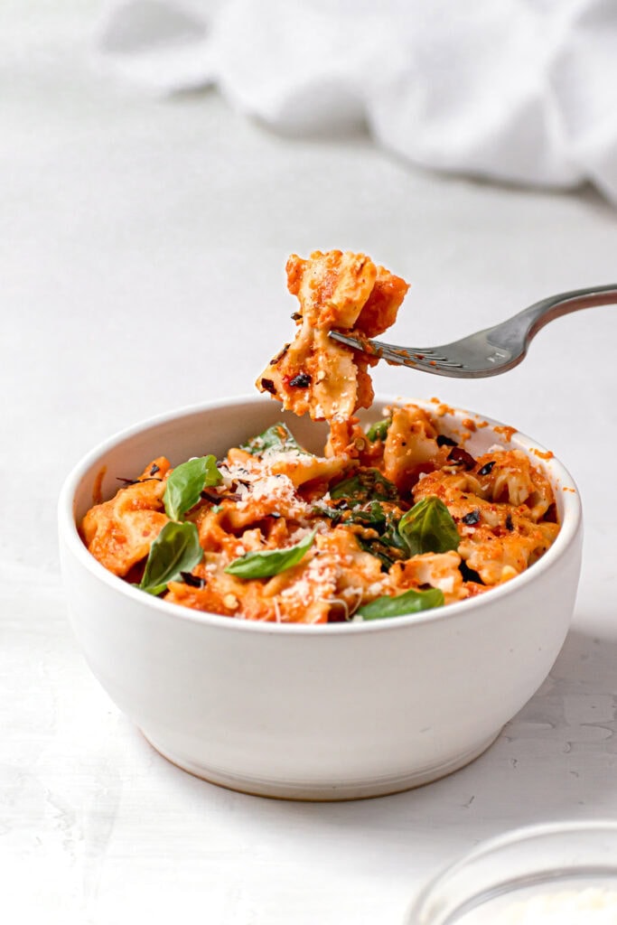 scoop of red pepper pasta on a fork over a bowl