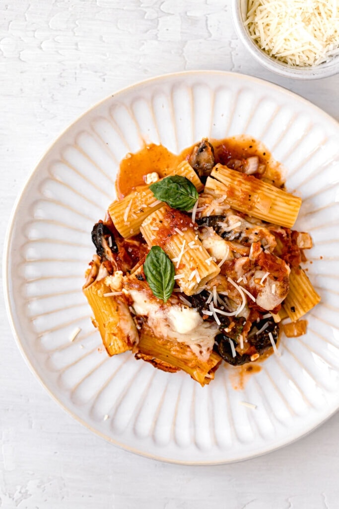 top shot of baked ziti on white plate next to parmesan cheese