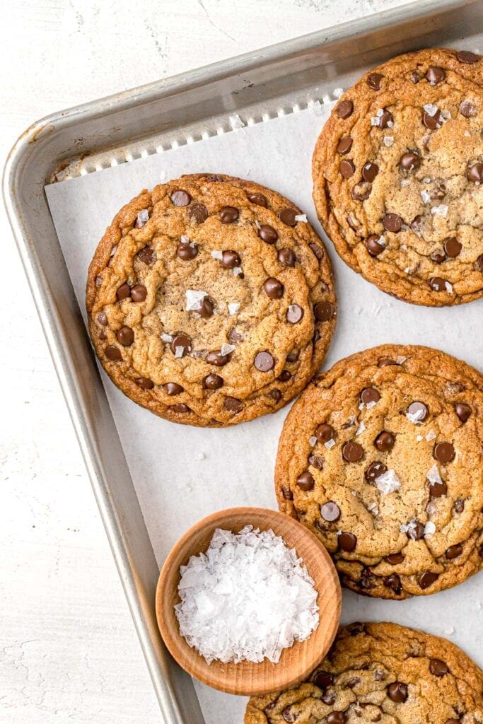 several chewy dairy free chocolate chip cookies on a baking sheet next to small bowl of sea salt