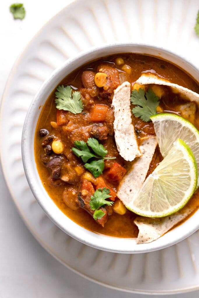 top shot of vegan taco soup in a white bowl topped with lime wedges
