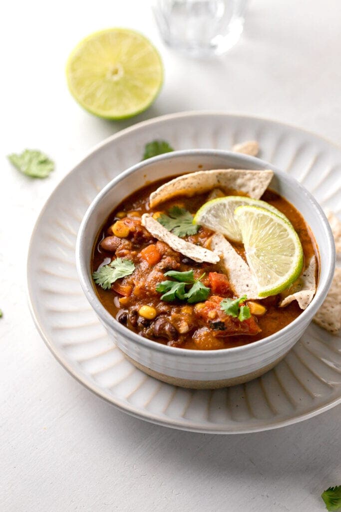 healthy vegan taco soup in a small white bowl on a plate with garnish