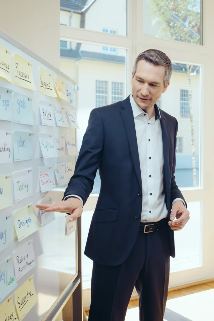 Michael Stockhausen, Geschäftsführer von Neuhaus Consulting steht an einem Whitboard und zeigt auf einen Klebezettel.