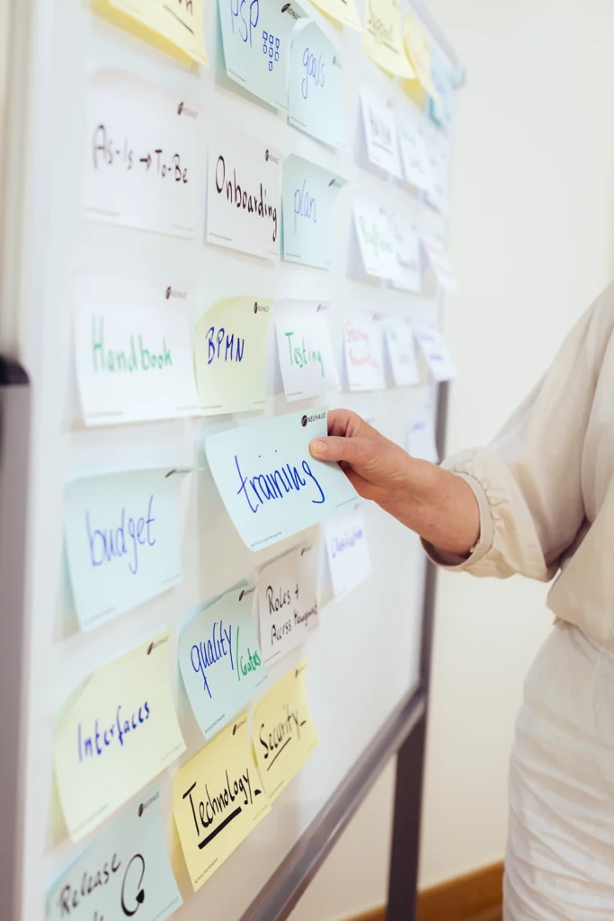 Eine Mitarbeiterin von Neuhaus klebt ein Post-it auf dem "training" steht an ein Whiteboard.