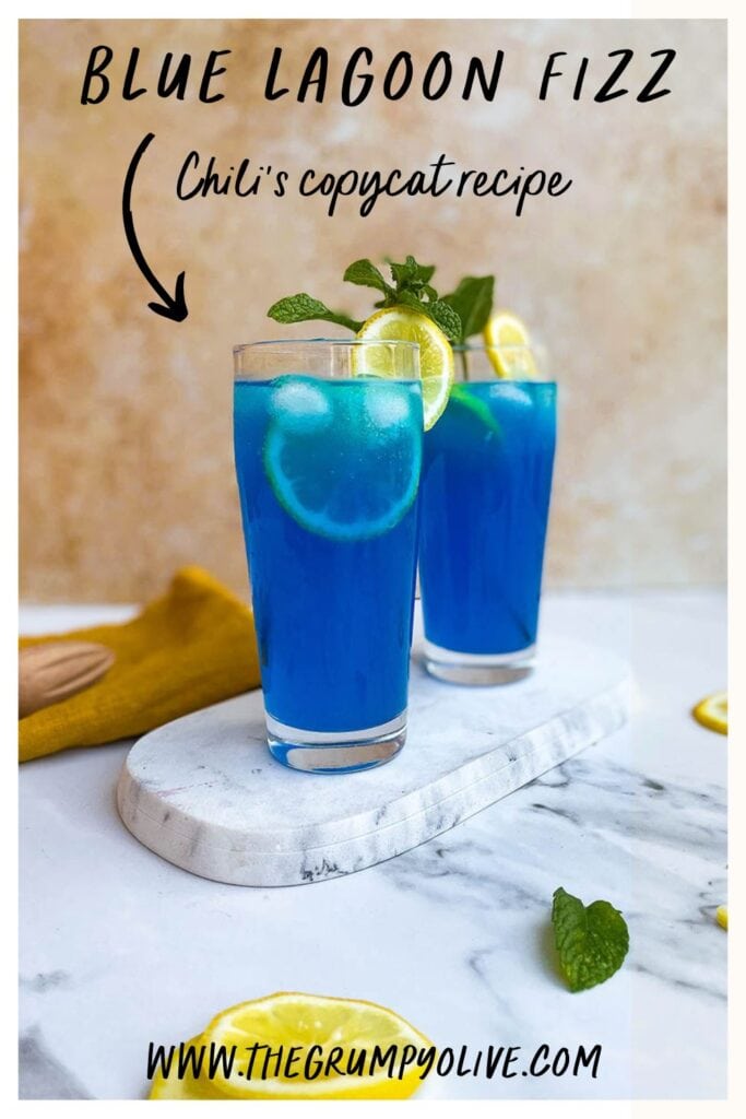 Summer Blue Lagoon Fizz Chillis Recipe Delicious Cocktail 6 two glasses of blue lagoon fizz chillis recipe on a marble slate with some lemon slices and mint leaves scattered around, a yellow napkin and a wooden citrus juicer with writing on top and bottom
