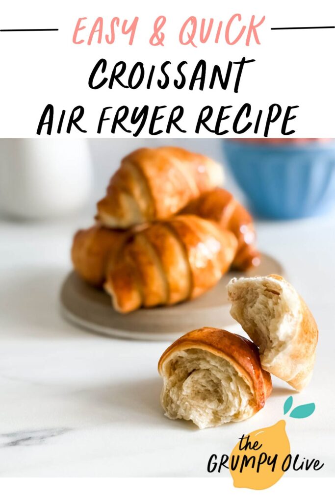 Croissant Air Fryer Recipe: Flaky, Delicious And Super Quick 8 A close-up of golden, flaky croissants with a glossy finish, one broken in half to reveal its soft, airy layers. The background features a blurred blue bowl and a milk jug. Overlaid text reads "Easy & Quick Croissant Air Fryer Recipe," with "The Grumpy Olive" logo in the bottom corner.