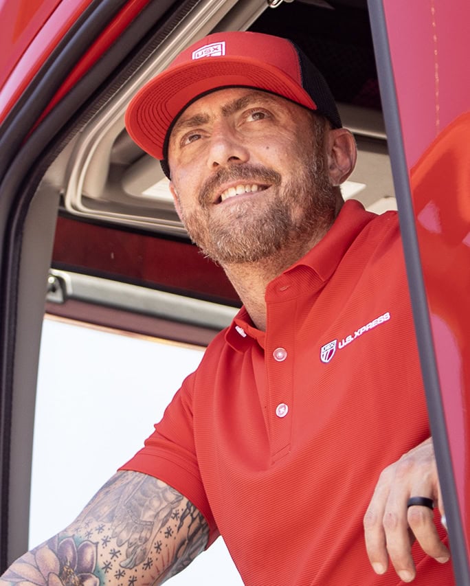 USXDR40858_Homepage Driver Portrait US Xpress driver with red shirt and hat on looks out of his truck.