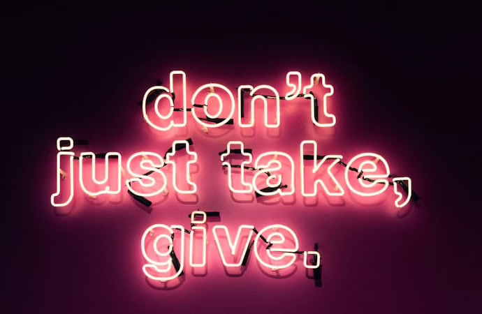 Neonlicht mit der Botschaft 'don't just take, give.' in pinker Schrift auf dunklem Hintergrund.