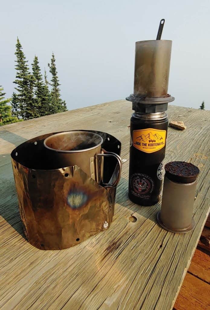 Camping stove and mug and aeropress coffee maker on a table in the mountains
