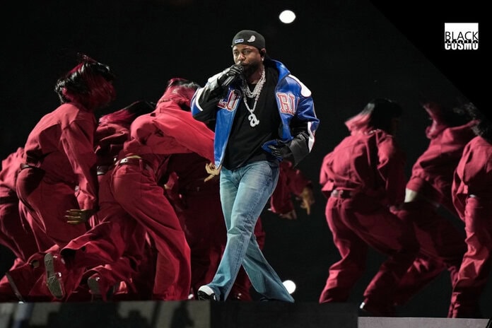 Kendrick Lamar performing during the Super Bowl LIX halftime show, surrounded by dancers in red and white, with Samuel L. Jackson appearing on stage in an Uncle Sam outfit.