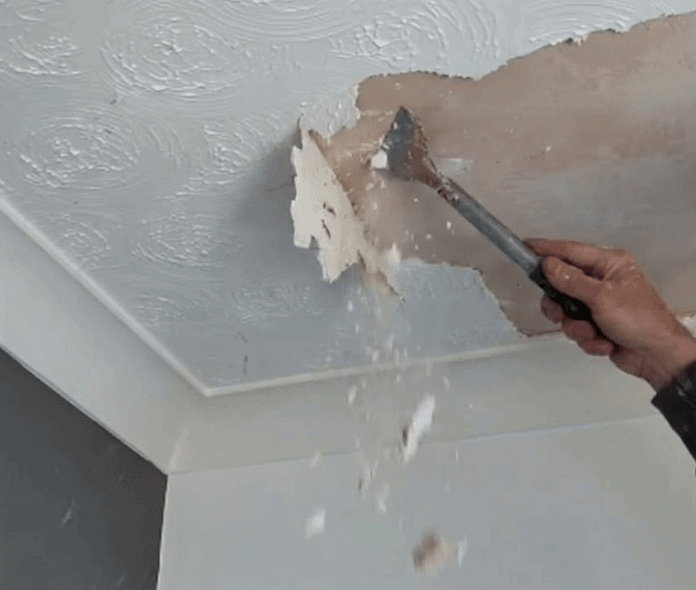 Hand scraping Artex textured coating from a ceiling during safe Artex ceiling removal in a Grantham property.