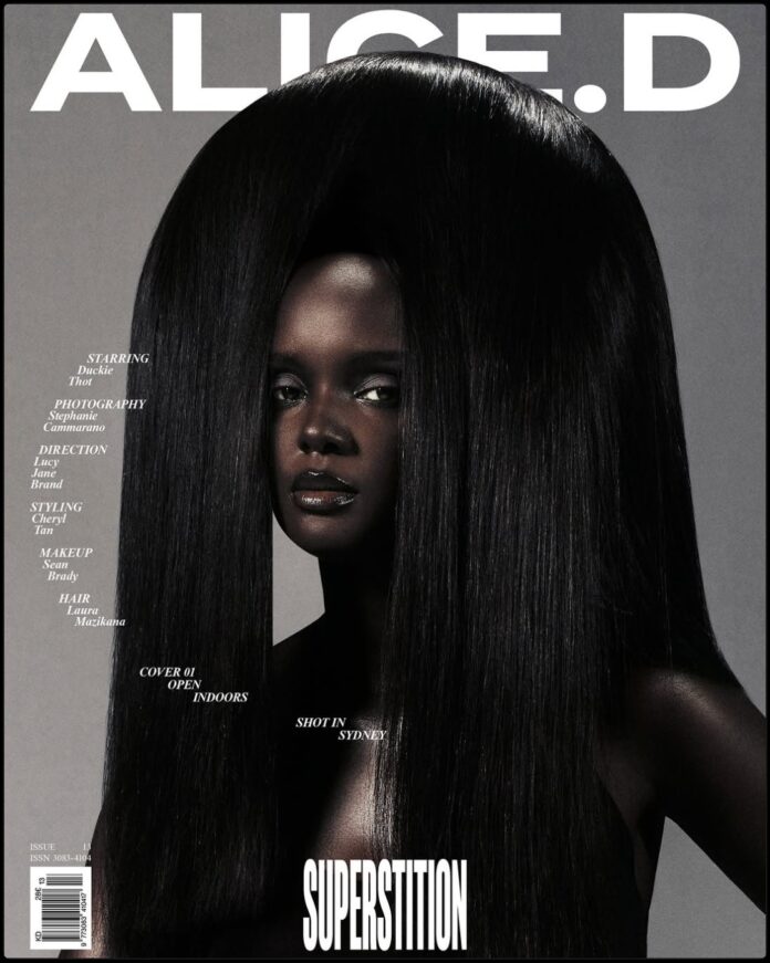 Duckie Thot on the cover of Alice'd Magazine wearing a bold red top and black skirt, posing confidently against an open city window.