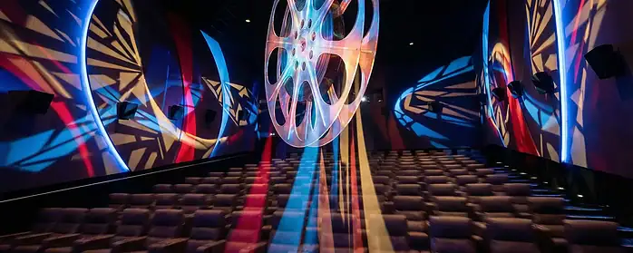 Abstract depiction of a cinema auditorium with vibrant lighting and a film reel.