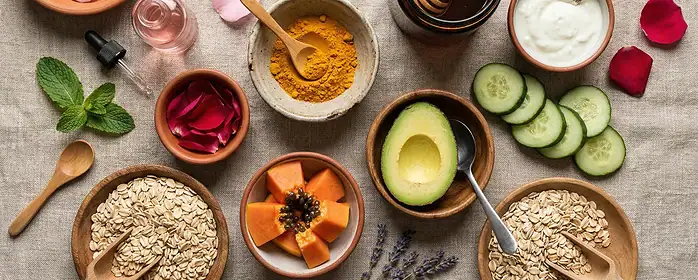 Homemade face mask ingredients like turmeric, honey, and yogurt in bowls surrounded by fresh citrus and cucumbers.