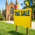 Colorful sign advertising a multi-family tag sale with details and people shopping in the background