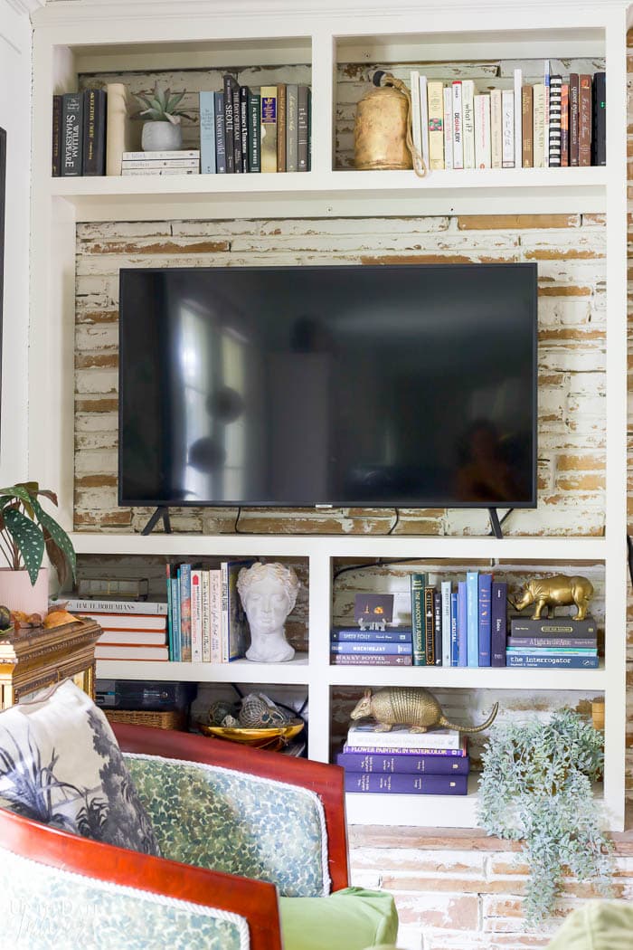 Built in bookcase with colorful books, brass figures, bust, large tv, and a green chair in front.
